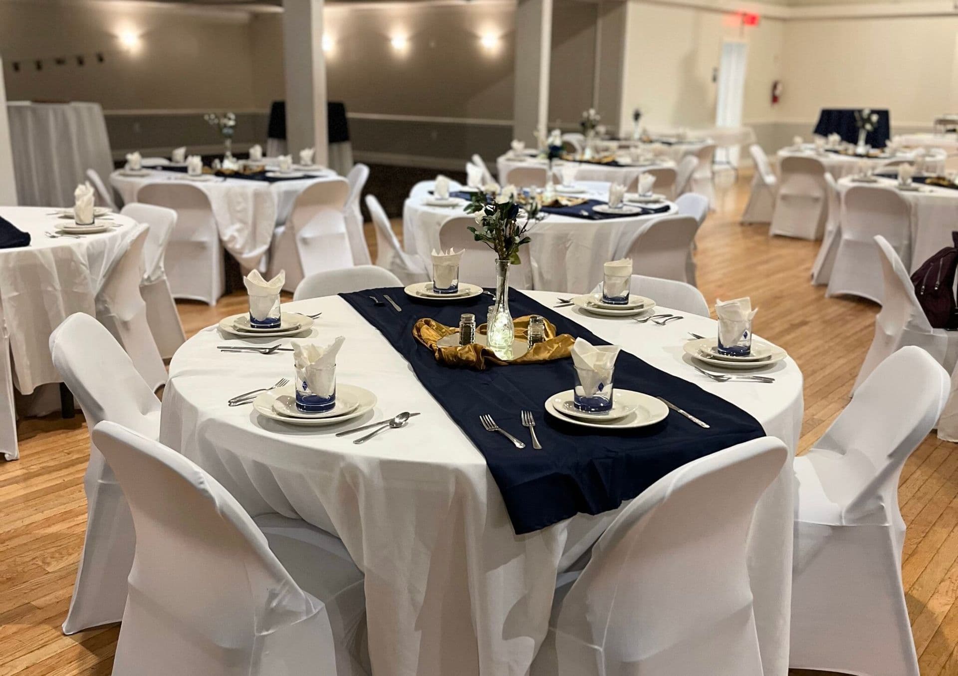 Ambassador Club Banquet Hall with white-covered round tables, navy runners, and a hardwood floor